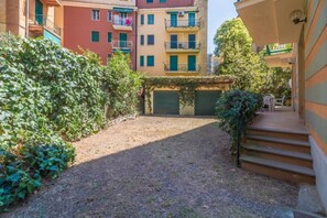 A courtyard with a gravel path, a green hedge, and a building with multiple balconies.