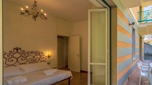 Une chambre à coucher avec un lit, un lustre et une porte-fenêtre coulissante donnant sur un espace extérieur aménagé avec des chaises.