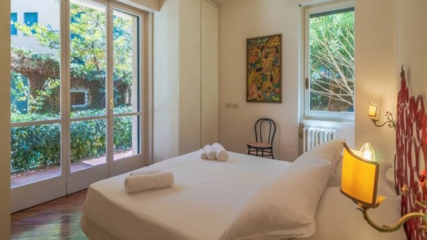 Une chambre à coucher avec un lit, une chaise, un tableau et une fenêtre donnant sur un paysage verdoyant.