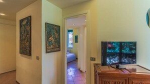 Un couloir orné d’œuvres d’art aux murs, avec un téléviseur et un lit en arrière-plan.