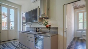 Cocina compacta con horno integrado, armarios de acero inoxidable y ventana con vista a un balcón.