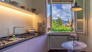 Een keuken met een raam, een radiator, een tafel met een vaas en een hanglamp.