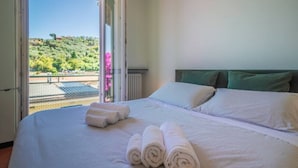 Een hotelkamer met een bed, kussens en uitzicht op een balkon met groen.