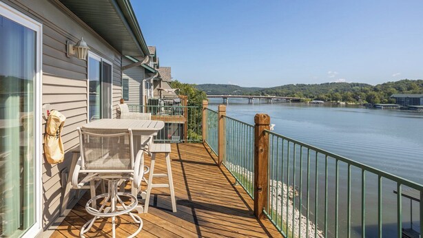 A wooden deck with outdoor furniture, a railing, and a view of a river and bridge.