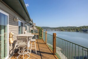 A wooden deck with outdoor furniture, a railing, and a view of a river and bridge.