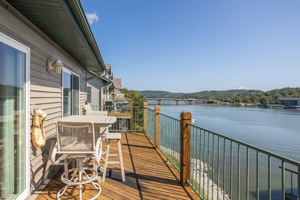 A wooden deck with outdoor furniture, a railing, and a view of a river and bridge.