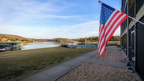 A flagpole with an American flag, a body of water, and a building with a dock.