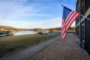 A flagpole with an American flag, a body of water, and a building with a dock.
