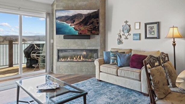 A living room with a fireplace, a large TV, and a balcony with a view of the ocean.