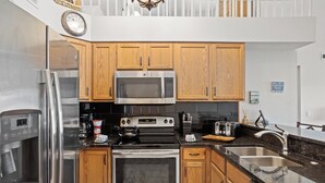 A modern kitchen with stainless steel appliances, wooden cabinets, and a black countertop.
