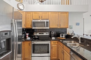 A modern kitchen with stainless steel appliances, wooden cabinets, and a black countertop.