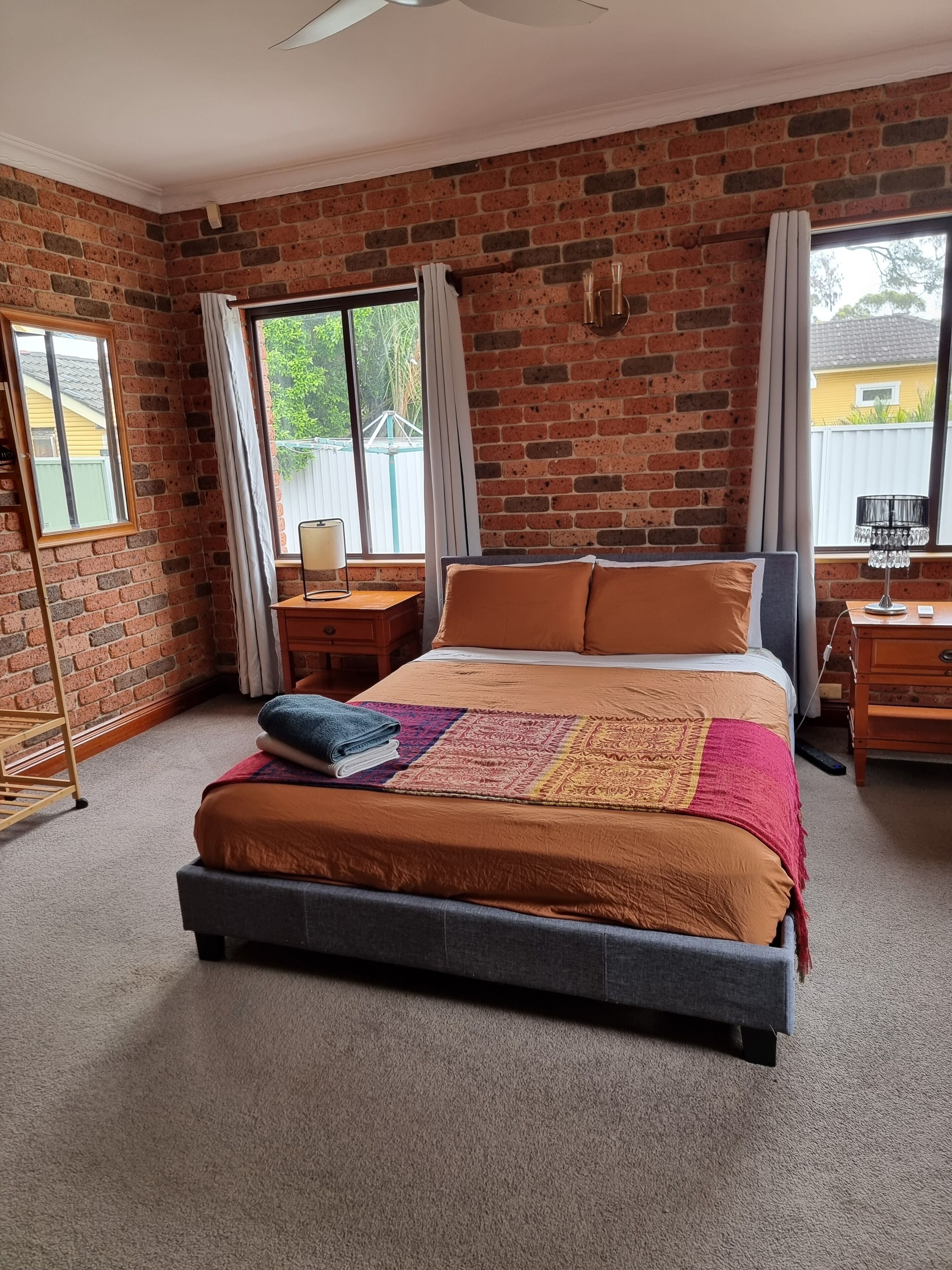 Un dormitorio con pared de ladrillo, una cama con colcha estampada, una mesita de noche, una lámpara y una ventana con cortinas.
