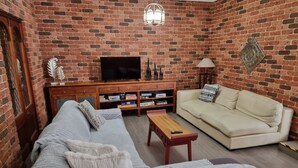 Una sala de estar con pared de ladrillo, un sofá, una mesa de centro, un televisor y un mueble con juegos de mesa.
