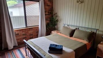 A bedroom with a brick wall, a window with curtains, a bed with a headboard, a bedside table, and a nightstand.