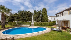 A swimming pool with a stone border, surrounded by a well-maintained lawn and a variety of trees. - CoolHouses Algarve Luz | Casa Sirrah (Luz)