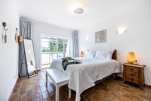 A bedroom with a bed, bedside table, bench, and a view of the outdoors. - CoolHouses Algarve Luz | Casa Sirrah (Luz)