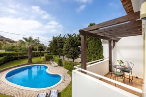 Une piscine avec une pergola et une table entourée de chaises sur un balcon.