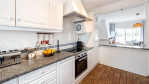 A modern kitchen with white cabinetry, a granite countertop, a Bosch kitchen scale, a fruit bowl, and a stove. - CoolHouses Algarve Luz | Casa Sirrah (Luz)