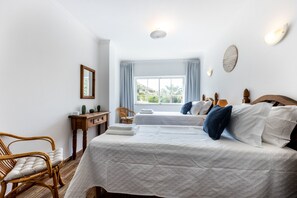 Ein Schlafzimmer mit einem großen Bett, einem Nachttisch, einem Sessel und einem Fenster mit Vorhängen.