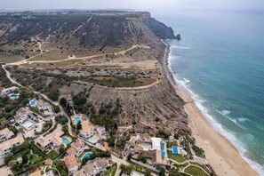 An aerial view of a coastal property with a beach, cliffside, and residential buildings. - CoolHouses Algarve Luz | Casa Sirrah (Luz)
