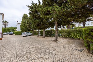 Une cour dallée, avec un sol en pavés, entourée d’arbres et d’une haie.