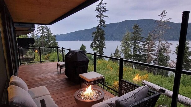 Une terrasse dotée d’un foyer extérieur, de coins salon et offrant une vue sur un lac et des montagnes.