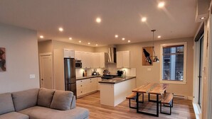 Une cuisine moderne avec des meubles blancs, un îlot central et un coin repas comprenant une table et des bancs en bois.