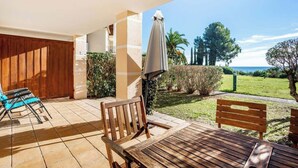 Une terrasse extérieure avec une table et des chaises en bois, un espace salon couvert et une vue sur la mer.