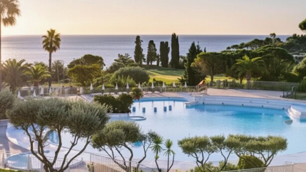Une piscine avec vue sur la mer, entourée d’arbres et d’une clôture.