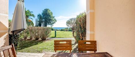 A patio with a table and two wooden chairs, a covered umbrella, and a view of a grassy area with trees and a clear sky.