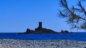 Une côte rocheuse avec une tour imposante qui se dresse sur une petite île, le tout étant entouré d’une eau d’un bleu limpide.