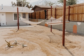Relax in a serene outdoor space with two hammocks suspended between poles, surrounded by a wooden fence and a rustic building.