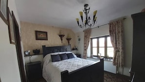 Een slaapkamer met een bed, een kroonluchter, een raam met gordijnen en een radiator.