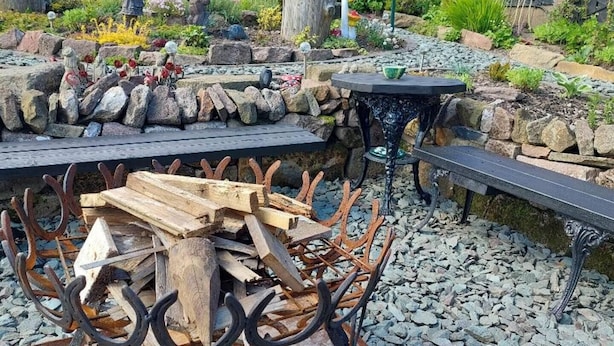 Een rustieke buitenruimte met een houten tafel en bankjes, omgeven door decoratieve stenen en planten.