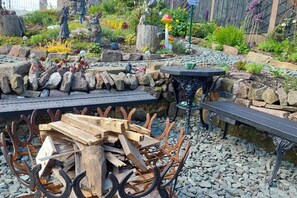 A rustic outdoor seating area with a wooden table and benches, surrounded by decorative stones and plants.