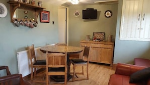 Een eethoek met een houten tafel en stoelen, een rode leren bank en een keuken met een televisie en kasten.