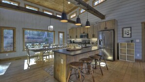 A spacious kitchen with wooden cabinets, a central island with stools, and a large refrigerator. - Modern 4BR Cabin w easy access, hot tub & a view! (Blue Ridge)