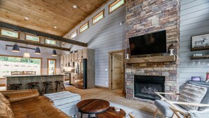 A spacious living area with a stone fireplace, leather sofa, and wooden accents. - Modern 4BR Cabin w easy access, hot tub & a view! (Blue Ridge)