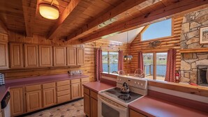 Une cuisine rustique aménagée dans une cabane en rondins, avec des meubles en bois, un poêle et une cheminée en pierre.