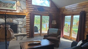 L’intérieur chaleureux d’un chalet avec une cheminée en pierre, un coin salon confortable et une vue sur un lac.
