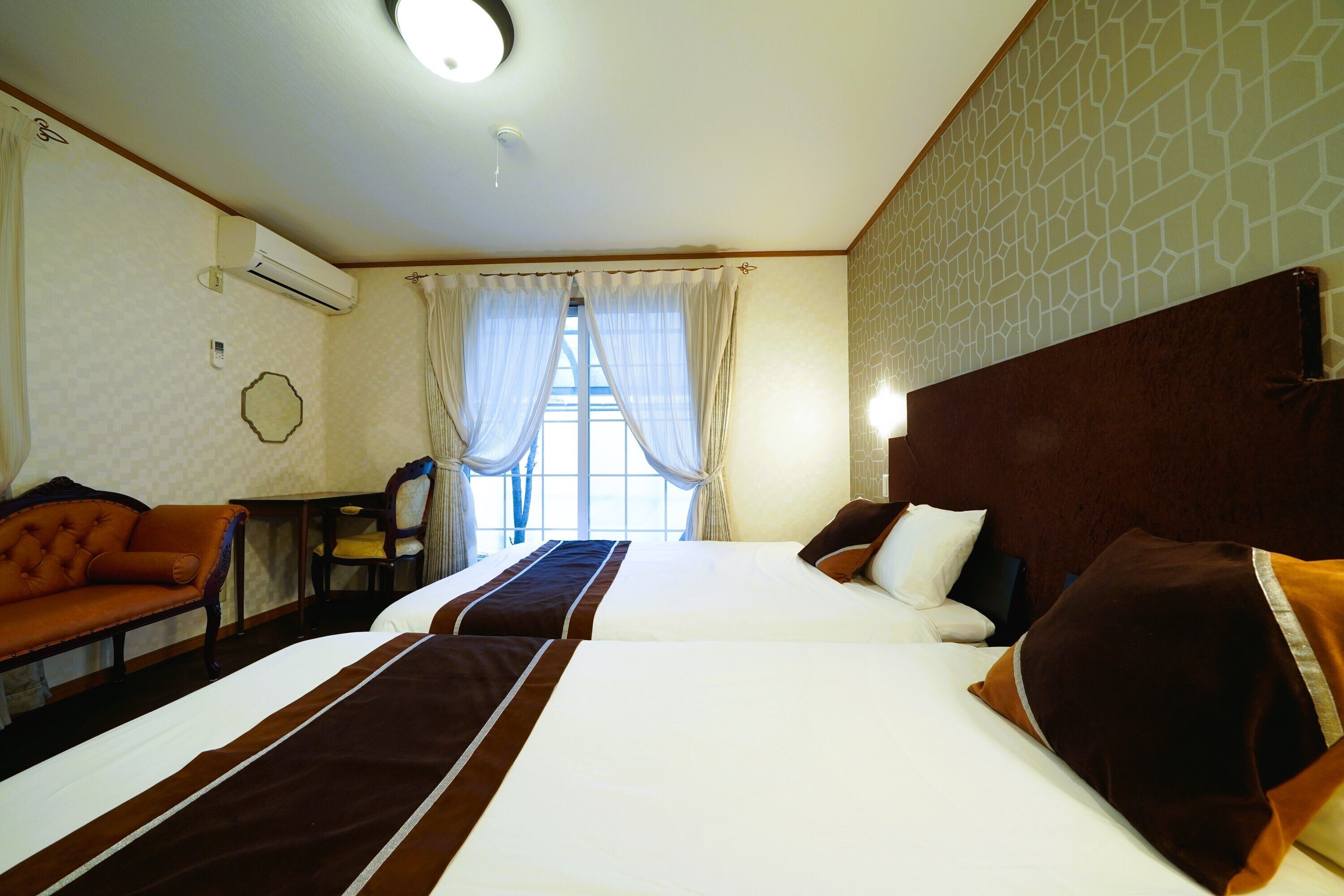 A hotel room with two beds, a sofa, a desk, and a window with curtains.