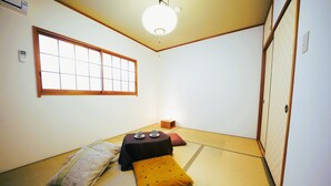 Ett traditionellt japanskt rum med tatamimattor på golvet, ett lågt bord med en kudde, ett fönster med träramar och en skjutdörr.