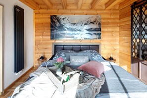 Habitación con paneles de madera, una cama, un cuadro de un paisaje montañoso, un radiador y una ventana con diseño de celosía.
