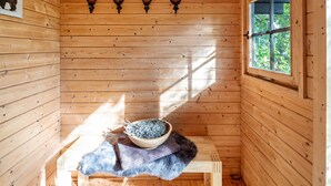L’intérieur d’un chalet en bois, avec une table en bois, un bol de graines, un tapis en fourrure et une fenêtre donnant sur les arbres.