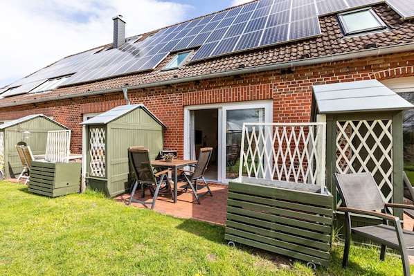 A house with solar panels, a brick exterior, a patio with a table and chairs, and a fenced garden area.
