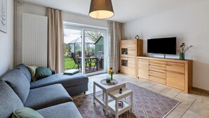 Un salon moderne avec un canapé, un téléviseur, un meuble en bois et une vue à travers la porte vitrée.