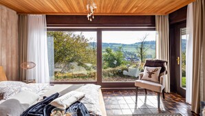 Une chambre avec une grande fenêtre, un lit, une chaise et une vue sur l’extérieur.