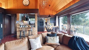 Un intérieur chaleureux avec un plafond en bois, un canapé en cuir, un coin cuisine et de grandes fenêtres.