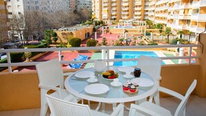 Ein Balkon mit einem runden Esstisch, der auf einen Pool und die umliegenden Gebäude blickt.