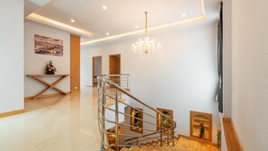 A modern interior with a staircase, wooden flooring, a chandelier, and a cityscape painting.